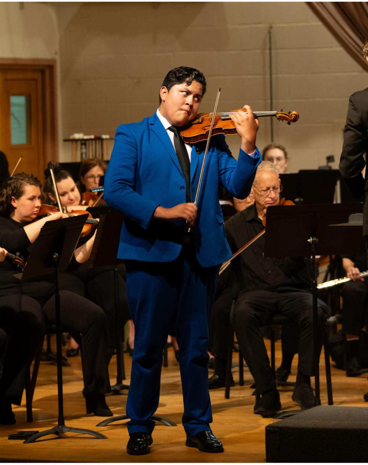 Jonathan Zapuche performing in a blue suit alongside the orchestra